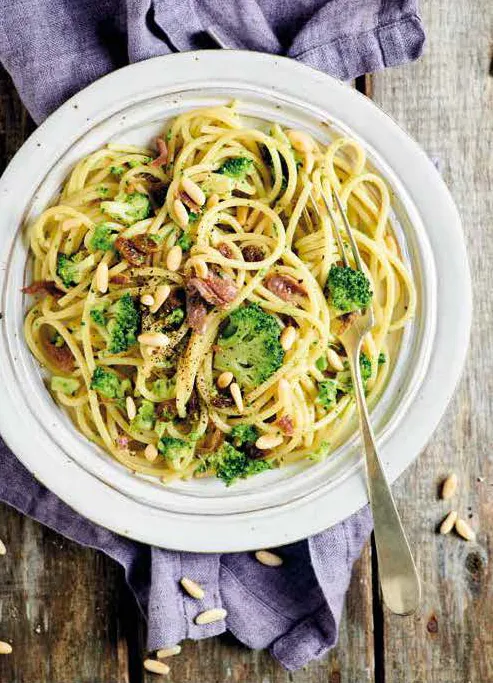 Fotografia del piatto di Spaghettoni con broccoli saltati, pinoli, acciughe e uvetta su una tavola apparecchiata